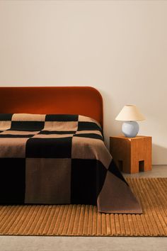 a bed sitting next to a lamp on top of a wooden table