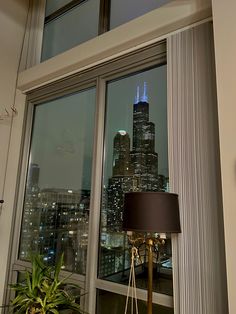 a lamp is on in front of a window with a view of the city at night