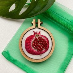 a red pomegranate in a wooden hoop hanging from a green ribbon on a white surface