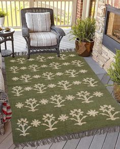 a green rug with white flowers on it in front of a chair and fire place