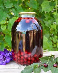 a glass jar filled with red berries sitting on top of a table next to purple flowers