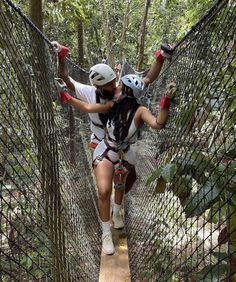 two people walking across a rope bridge in the forest