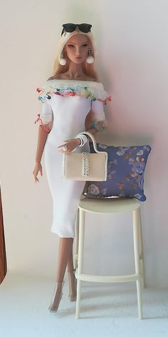 a doll is sitting on a chair with a purse in front of her and a handbag behind her