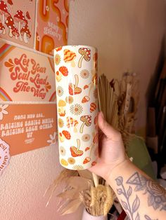 a person holding up a paper cup in front of a wall with stickers on it