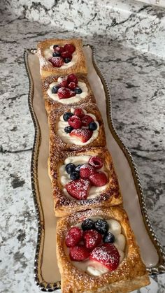 four desserts are lined up on a platter with berries and powdered sugar