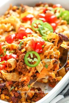 a casserole dish filled with chili, cheese and green peppers is being lifted by a spoon