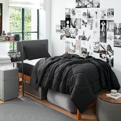 a bed with black comforter and pillows in a white room next to a window