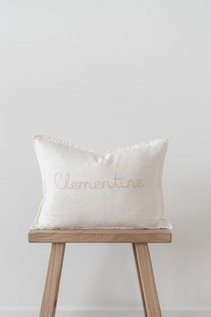 a white pillow with the word clementne on it sitting on a wooden stool in front of a white wall