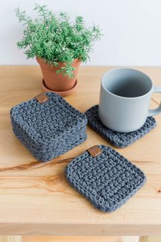 two crocheted coasters on a wooden table with a coffee cup and plant