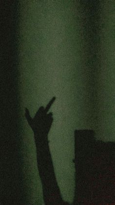 the shadow of a person's hand in front of a green wall with light coming through it