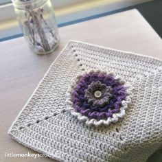 a crocheted square sitting on top of a table next to a vase filled with flowers