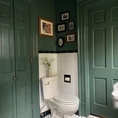 a white toilet sitting in a bathroom next to a green wall with pictures on it