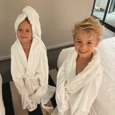 two children wrapped in white towels sitting on a bed