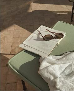 an open book with sunglasses on top of it sitting on a chair next to a towel