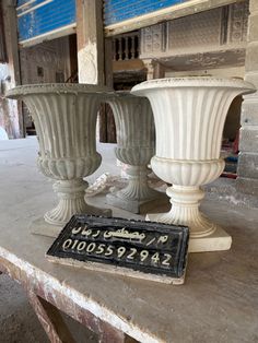 two large white vases sitting on top of a wooden table next to a sign