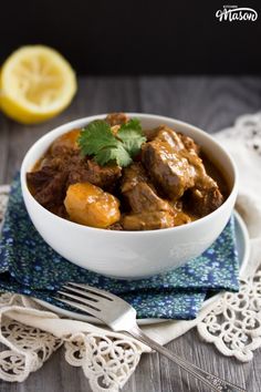 a white bowl filled with stew next to a slice of lemon on top of a blue and white napkin