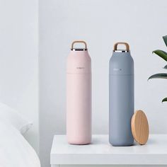 two insulated water bottles next to a potted plant on a white shelf in a bedroom