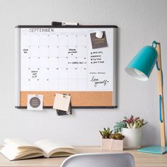 a desk with an open book, lamp and calendar on the cork board attached to the wall