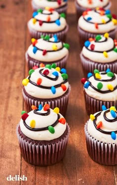 cupcakes decorated with white frosting and multi colored sprinkles on a wooden table