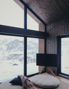 there is a round pillow on the floor in front of two large windows with snow outside