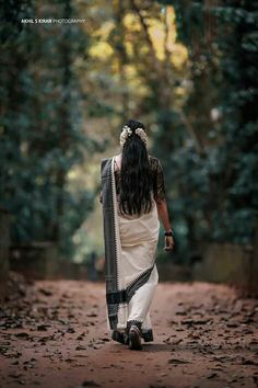 a woman walking down a dirt road with trees in the background