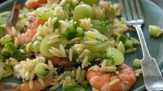 a green plate topped with shrimp and rice salad next to a fork on a table