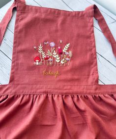 a red apron with embroidered flowers on the front and words below it that says, delight