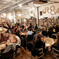 a group of people sitting at tables eating food in a room with bookshelves