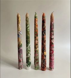 four different colored candles are lined up in the same row and one is painted with flowers