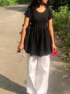 a woman in black shirt and white pants holding flowers on the side of a road