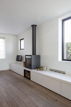 a living room with white walls and wood flooring, a black fire place in the center