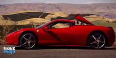 the red sports car is parked on the side of the road with mountains in the background