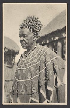 an old black and white photo of a woman in native dress standing next to some huts