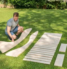 a man kneeling down next to some wooden boards on the grass in front of a tree