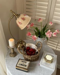 a table topped with a basket filled with strawberries next to a lamp and books