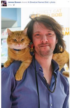 a man is holding a cat on his shoulders and smiling at the camera while wearing a blue shirt