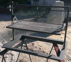 a grill sitting on top of a wooden table in the sand next to a large rock