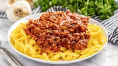 a white bowl filled with spaghetti and meat sauce on top of a marble countertop