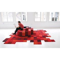 a man sitting on top of a red and purple rug in an empty room with windows