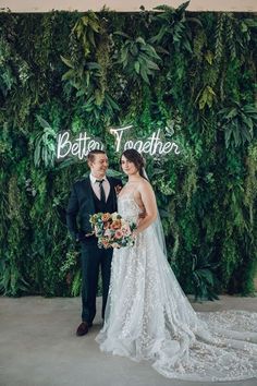 a bride and groom standing in front of a green wall with the words better together