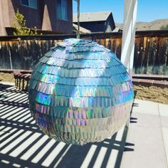 a disco ball sitting on top of a sidewalk next to a fence and building in the background