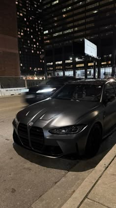 two cars parked on the side of a street at night with buildings in the background