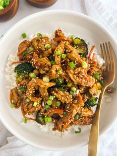 a white plate topped with chicken and broccoli covered in sesame seed sauce next to rice