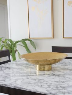 a bowl sitting on top of a marble table in front of two framed art pieces