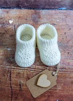 a pair of white knitted baby shoes next to a tag with a heart on it