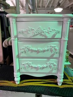 a white dresser with green paint on it's drawers in a room filled with other furniture