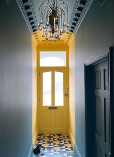 an empty hallway with a yellow door and chandelier hanging from it's ceiling