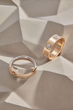 two wedding rings sitting on top of a white and gold paper covered surface with diamond accents