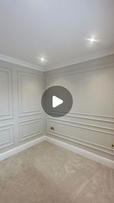 an empty room with white paneling and beige carpeted walls in the corner, there is a video play button on the wall