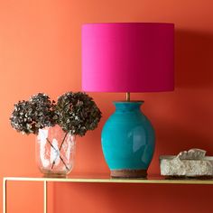 a blue vase sitting on top of a table next to a pink lamp and rocks